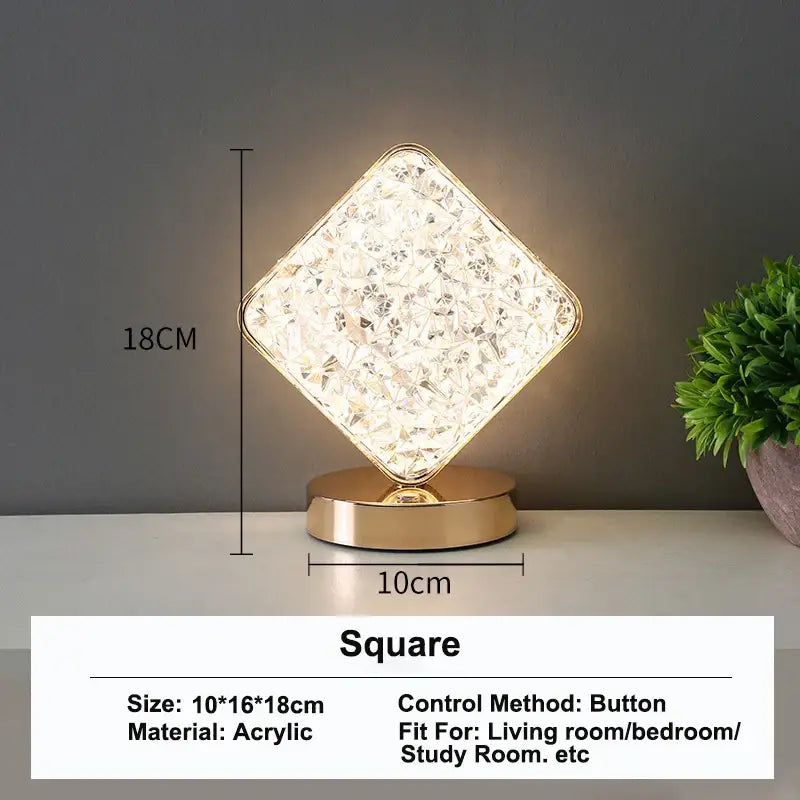A square gold-accented acrylic table lamp with faceted crystal surface and touch dimming night light function emitting warm white light