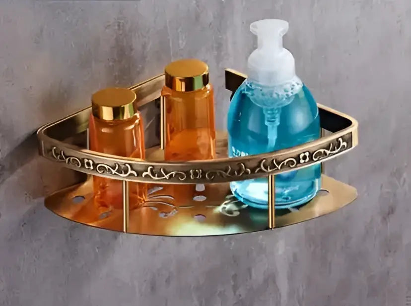 Gold-toned triangular bronze carved bath shelf with ornate scrollwork holding amber bottles and blue soap dispenser
