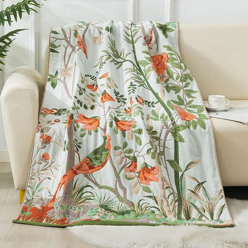 A soft light blue decorbites cotton gauze bath towel with vibrant orange birds and green foliage botanical print