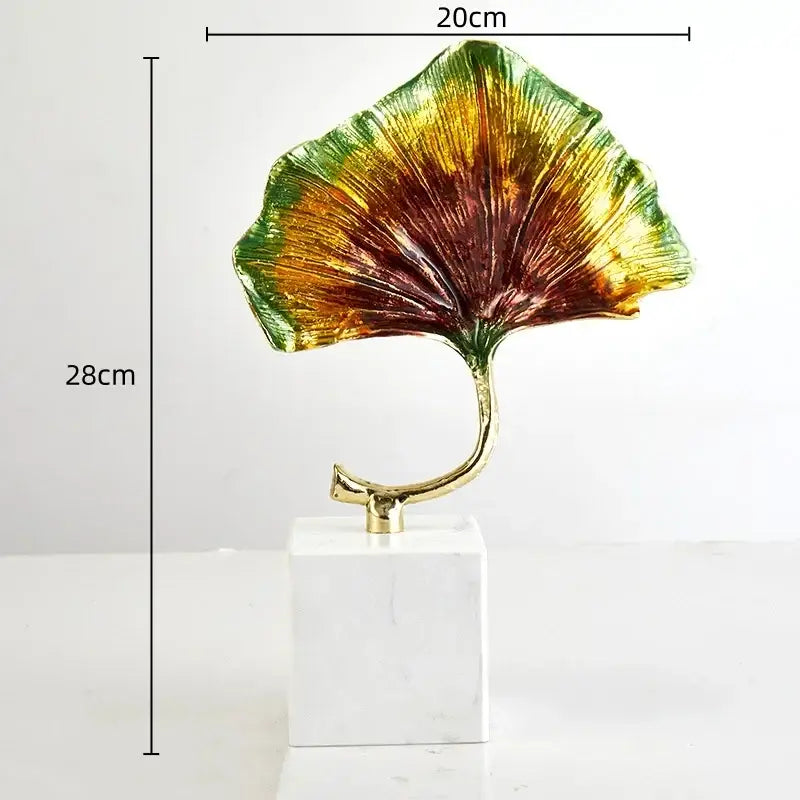 Vibrant iridescent decorbites ginkgo leaf metal sculpture with a golden stem on a white marble base for home decor