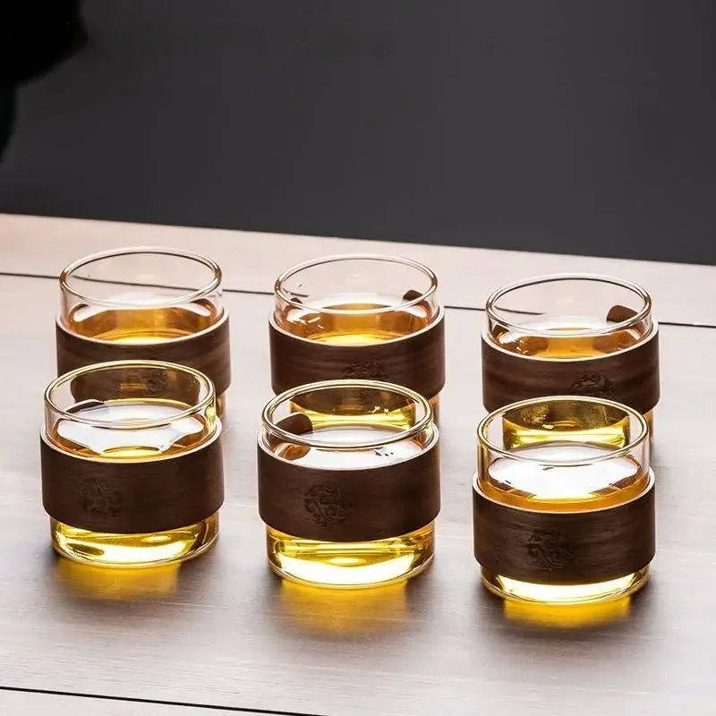 Set of six clear glass teacups with dark brown wooden bands holding amber liquid from decorbites glass teapot set