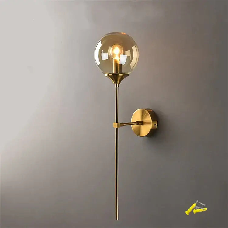 A sleek brass decorbites glass wall lamp with a spherical amber glass globe for bedroom lighting