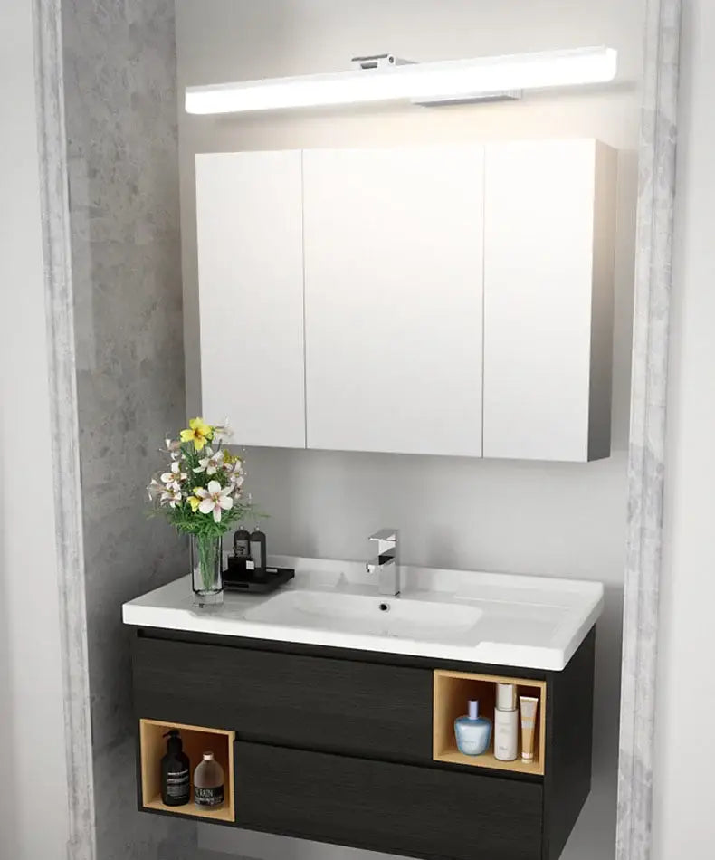 Modern rectangular acrylic golden mirror cabinet light above white and dark wood bathroom vanity with open shelving