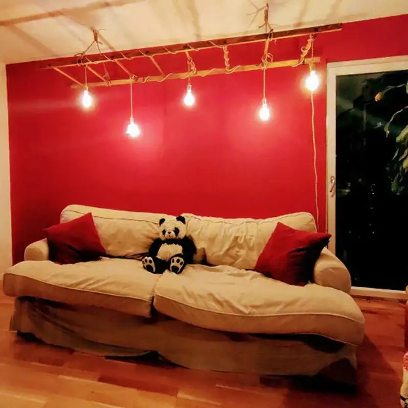 Rustic beige hemp rope pendant light cable above beige upholstered sofa with red pillows and black-and-white panda toy