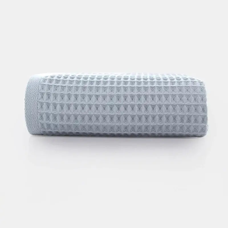 A neatly rolled soft gray cotton waffle towel with a textured grid pattern from decorbites cotton waffle bath set