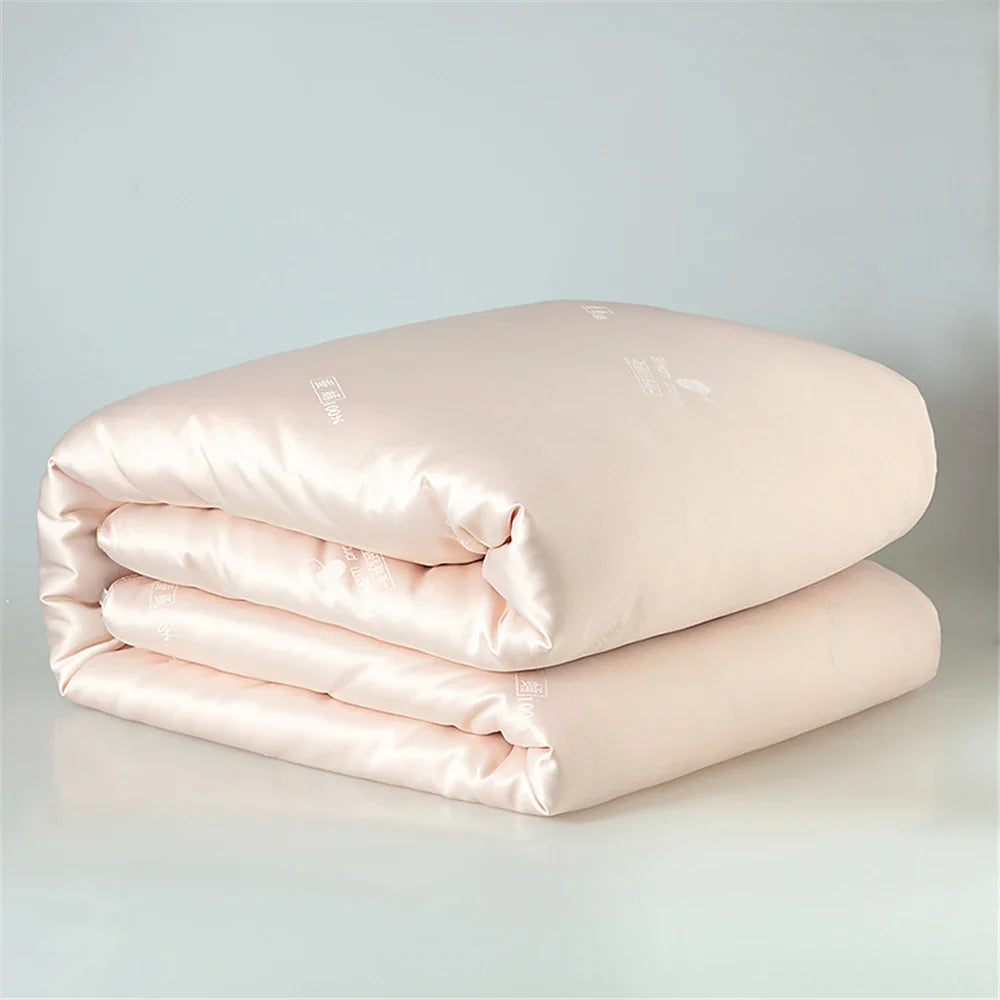 A soft blush pink satin silk quilt with subtle sheen and delicate embroidered branding for luxurious sleep