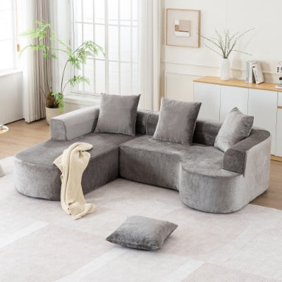 Gray velvet sectional sofa with matching throw pillows and cream blanket draped over one armrest in sofas collection.