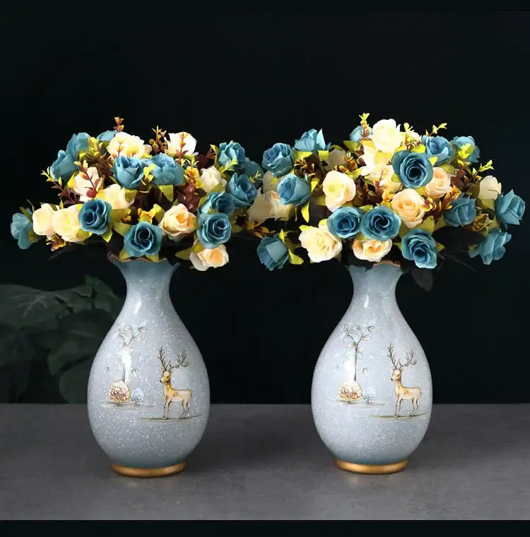 Pair of light blue ceramic vases with gold-trimmed bases and deer illustrations holding dried flowers bouquets