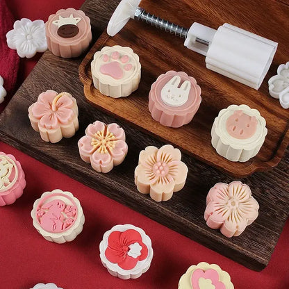 Pastel pink and cream 3d cherry blossom mooncake molds with floral animal and heart designs on wooden tray for baking