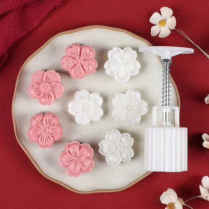 White and pink flower-shaped cherry blossom mooncakes on a speckled plate next to a white plastic decorbites 3d cherry mold