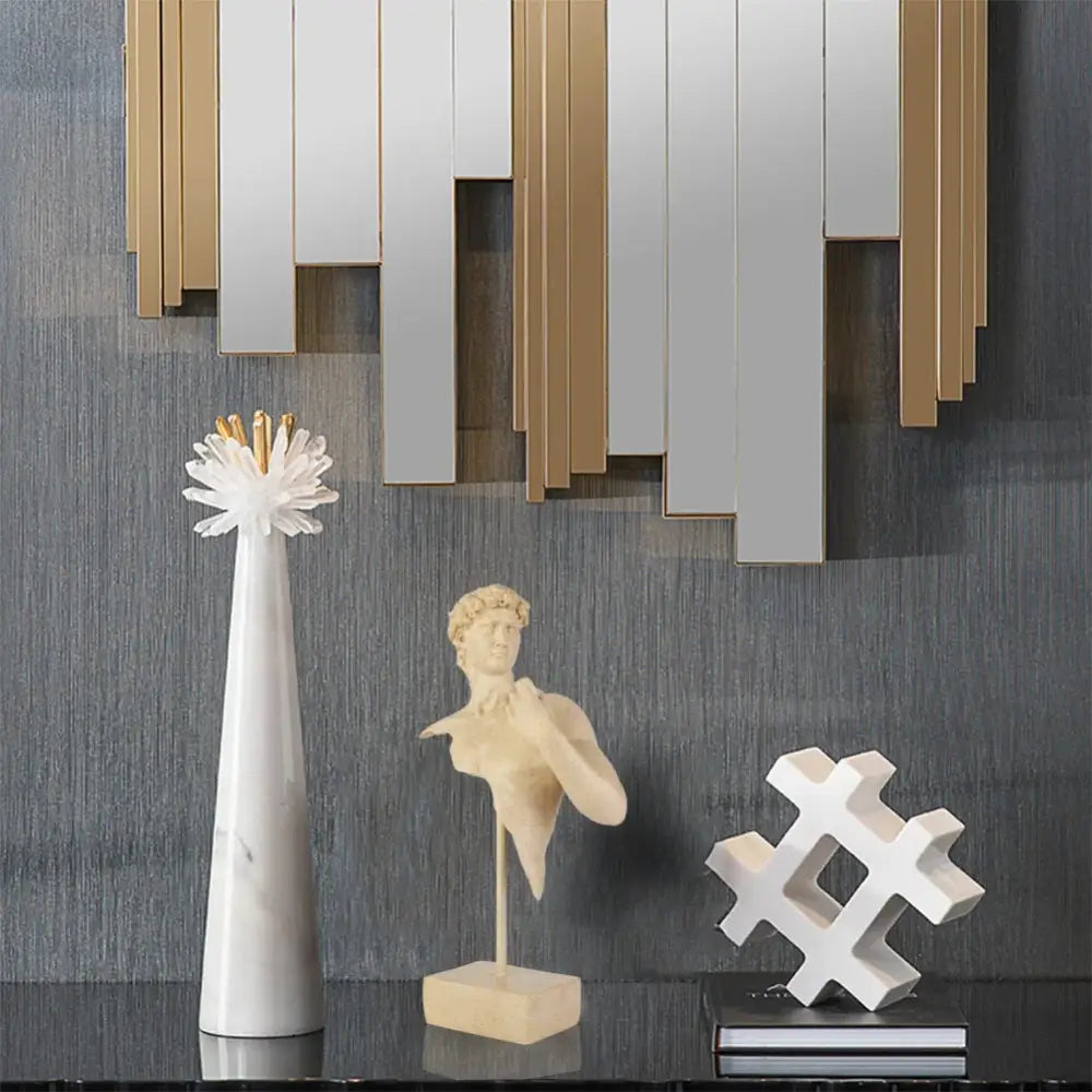 White marble vase with gold-tipped floral arrangement beside abstract beige david bust resin sculpture for living room decor