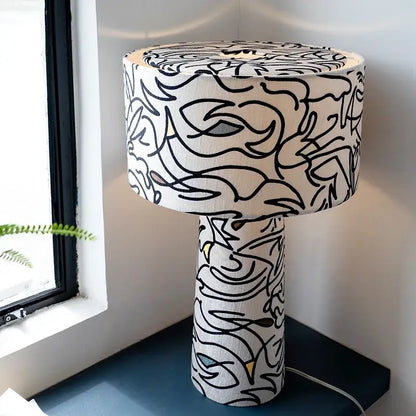 A cylindrical study lamp with white fabric shade and base featuring bold black abstract line art decorbites designer french medieval