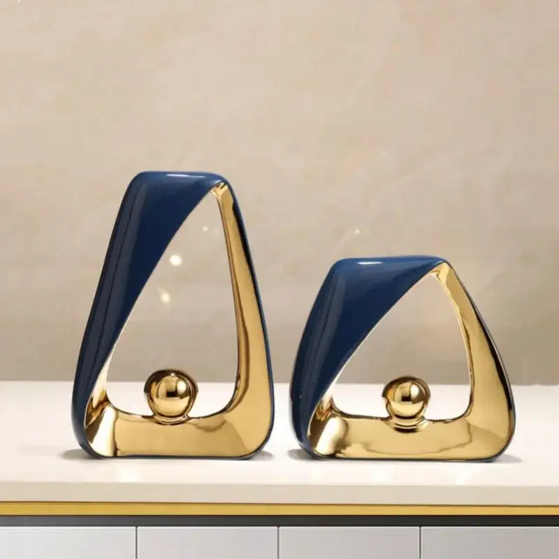 Two modern ceramic sculptures with navy blue and gold geometric triangles and a polished golden ball for home decor