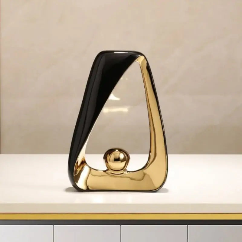 A sleek abstract black and gold geometric triangles sculpture with a golden ball for modern home decor