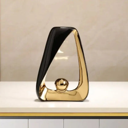 A sleek abstract black and gold geometric triangles sculpture with a golden ball for modern home decor