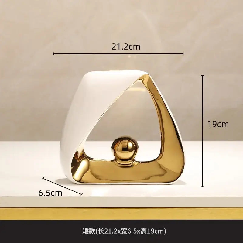A sleek ceramic abstract sculpture with white and gold geometric triangles and a polished golden ball for home decor
