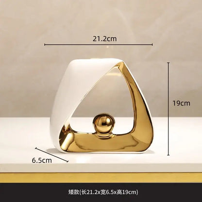 A sleek ceramic abstract sculpture with white and gold geometric triangles and a polished golden ball for home decor