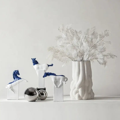 White ceramic vase with ribbed texture holding white dried foliage next to abstract black and gold decorbites horse statue