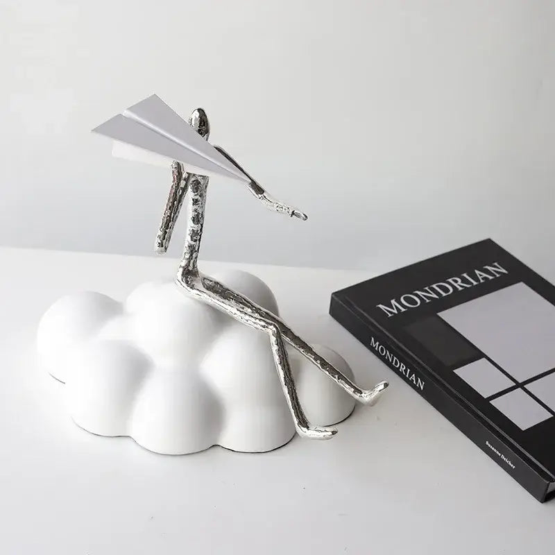Silver metallic abstract figurine sitting on white resin paper airplane cloud holding paper airplane for living room decor