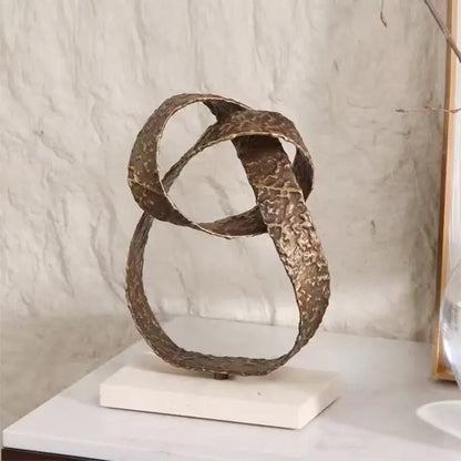 Bronze-colored textured metal geometric sphere pendant sculpture with interlocking loops on white marble base for decor
