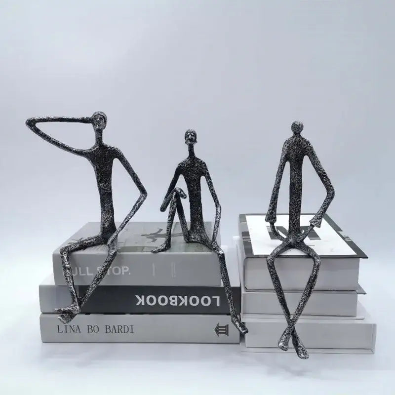Three abstract metal human sculptures with textured dark gray bronze finish posed on stacked books for living room decorbites abstract metal decor
