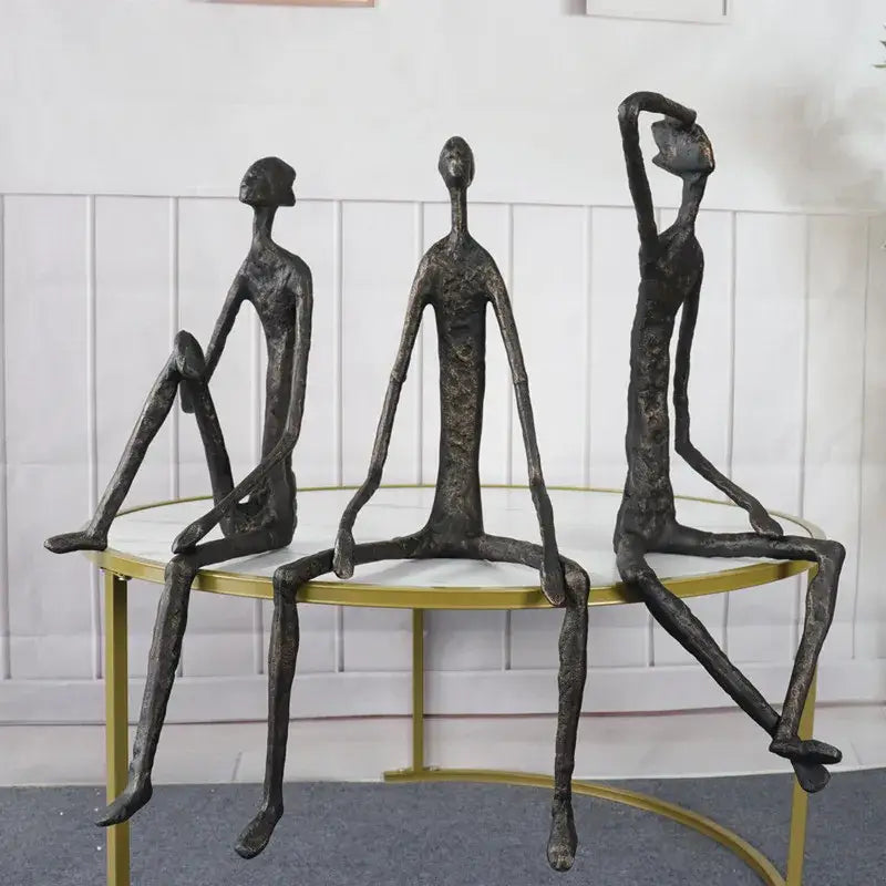 Three abstract bronze-colored metal human sculptures with elongated limbs seated on a round table decorbites abstract metal decor