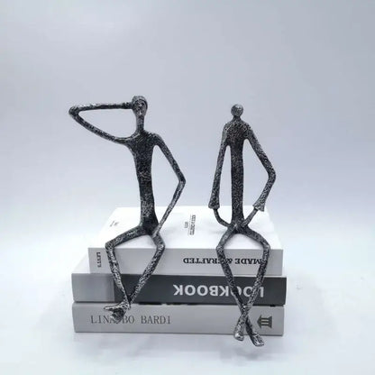 Two abstract bronze metal human sculptures in black textured finish sitting atop books for living room decorbites abstract metal decor