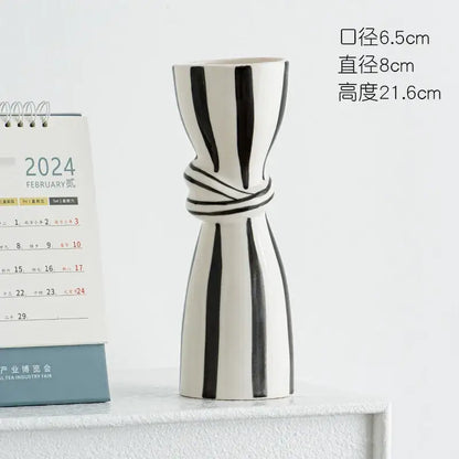 A sleek white abstract ceramic hydroponic vase with bold black stripes and a twisted band around its midsection