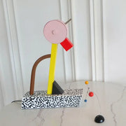 Abstract duck led table lamp with vibrant pink circular top yellow rod red rectangular piece and black triangular base