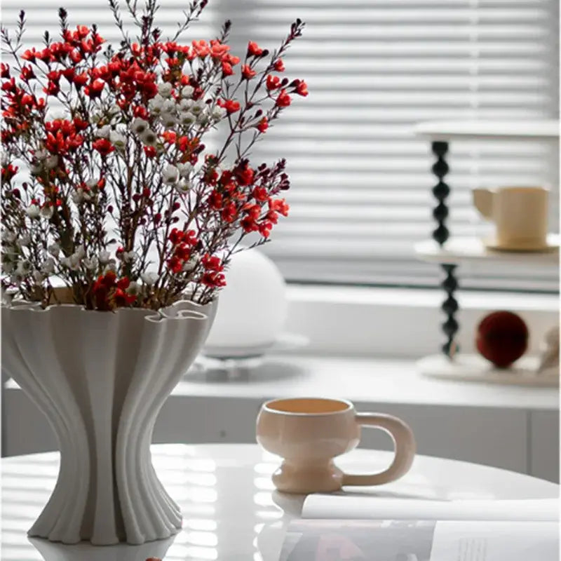 A white fluted ceramic abstract geometry vase with triple openings holds red and white dried flowers for living room decor