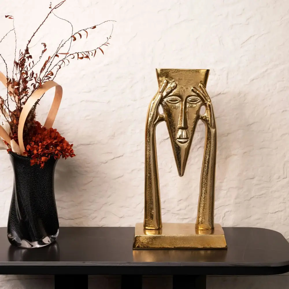 Golden masked figure sculpture with elongated face and hands on square base for living room decor