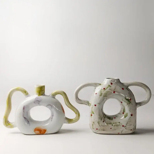 Two ceramic vases with abstract handle ceramic design and hand-painted floral accents in muted green and red decorbites abstract handle