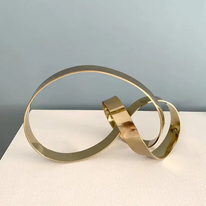 Gold-toned metallic abstract knot sculpture with interlocking circular bands for living room decor by decorbites