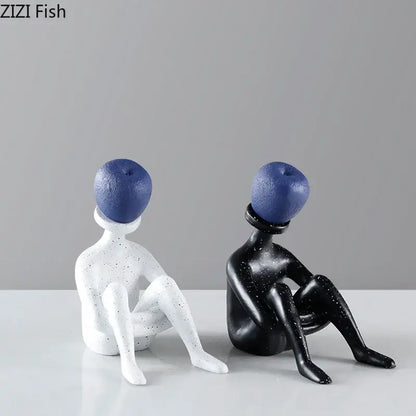 Two minimalist abstract thinker resin figurines with speckled black and white bodies and blue apple heads for decorbites decor