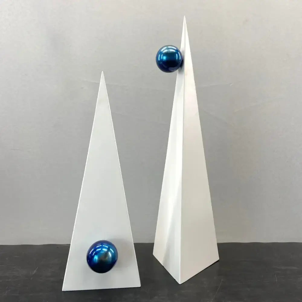 Two minimalist white geometric triangle sculptures topped with glossy blue spheres for decorbites geometric triangle decor