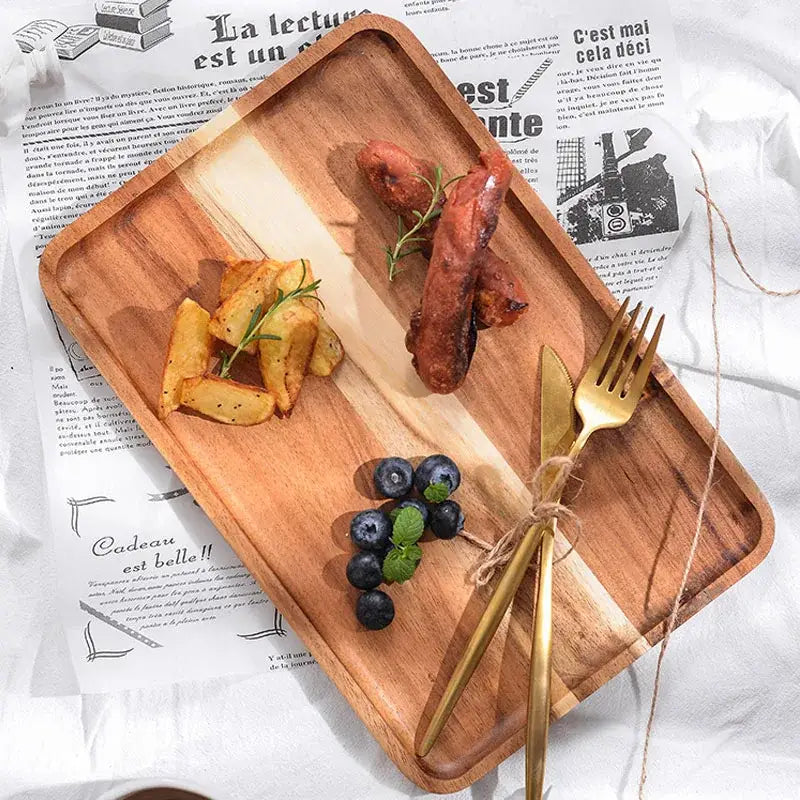 Rectangular acacia wood breakfast tray with natural wood grain, rounded edges, grilled sausages, potatoes, blueberries, and gold cutlery
