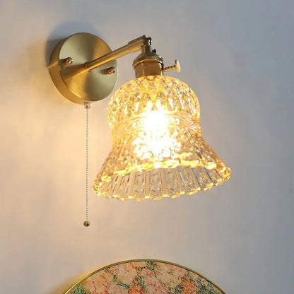 Vintage-style brass wall light fixture with faceted bell-shaped amber flower crystal glass shade and pull chain for bedroom