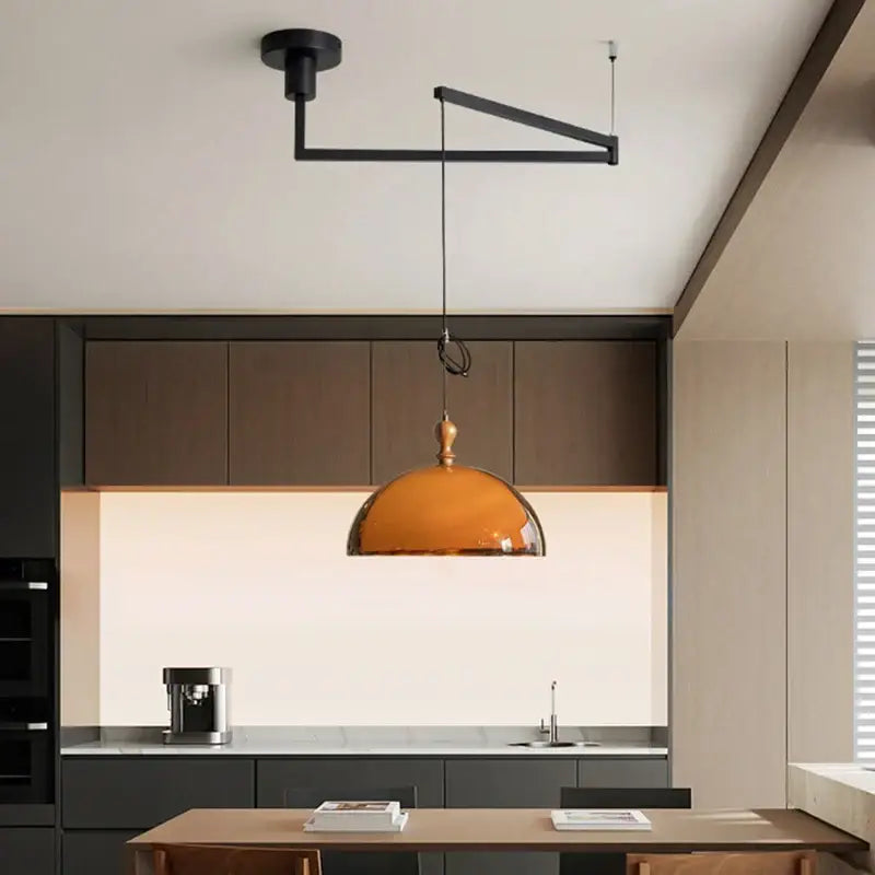 A sleek amber glass pendant light with a polished brass fixture and dark wood accent for dining rooms