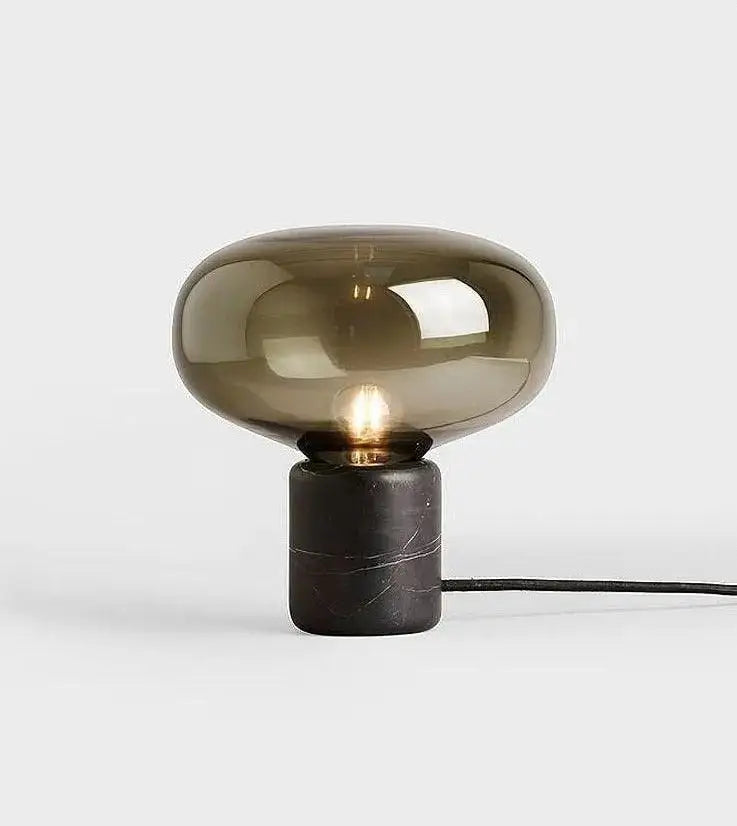 A nordic table lamp with a rounded amber glass shade and a dark marble base for modern interiors