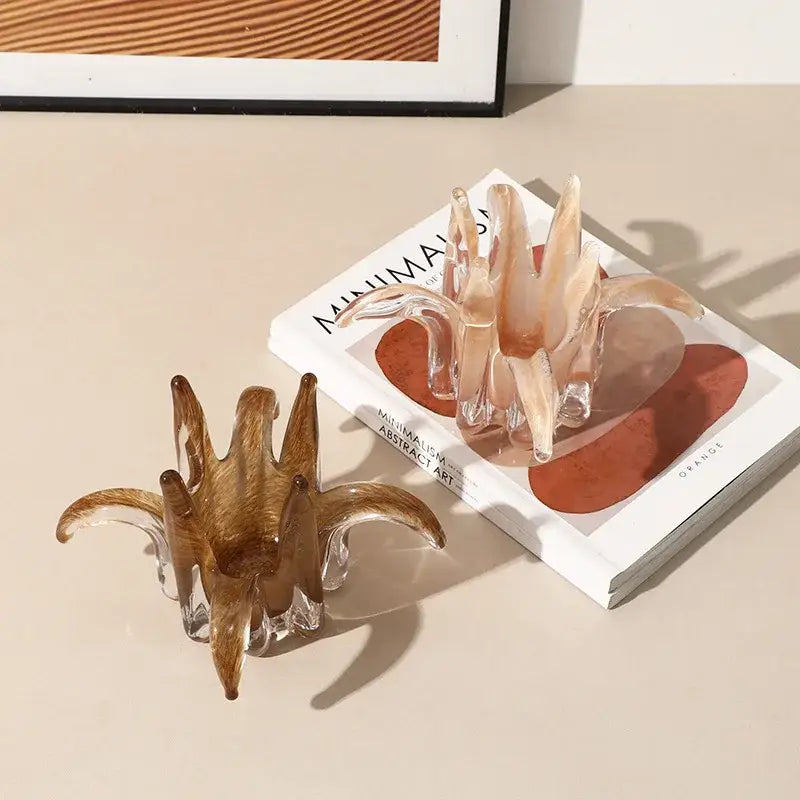 Two translucent sculptural hair clips in amber and peach with glass-like finish shown alongside glass petal candle holder decor