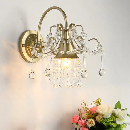 Antique brass wall light sconce with crystal teardrop accents and intricate filigree detailing for bedroom use