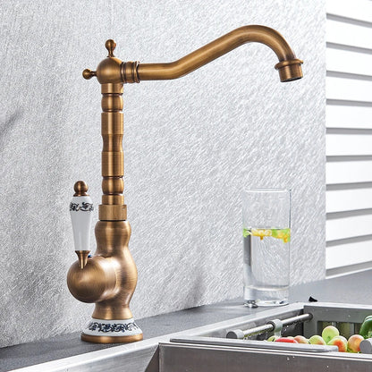 Antique brass basin faucet with white ceramic handle featuring black floral detailing and ornate base trim