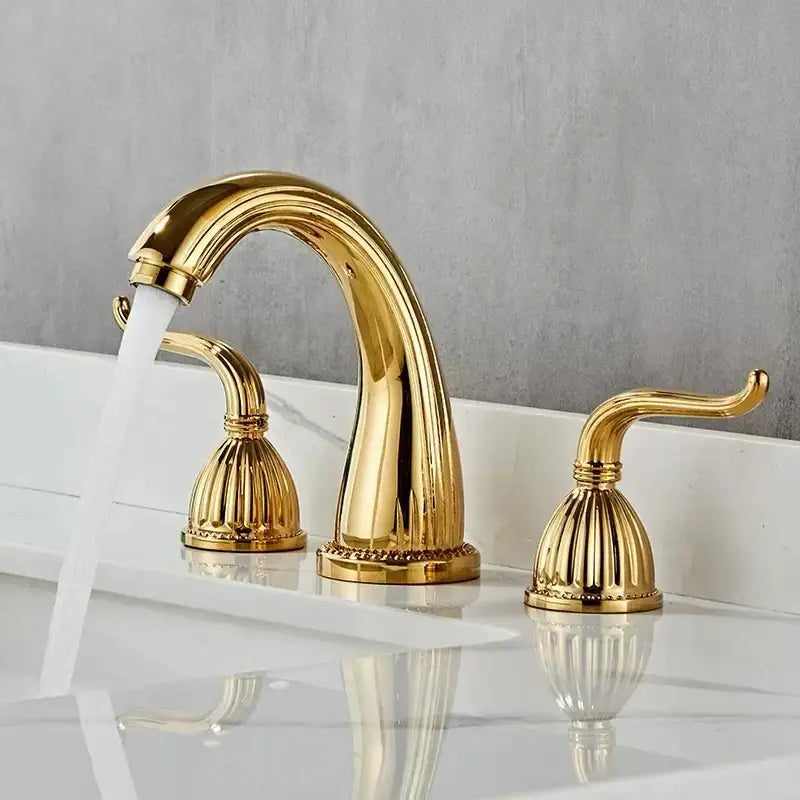 Antique brass bathroom faucet set with gold-finished ornate three-handle design and curved spout with fluted handles