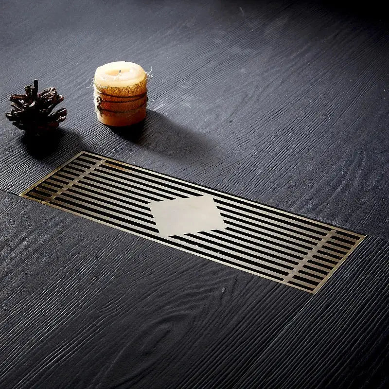 A sleek rectangular floor drain cover with a brushed metallic finish and parallel slats for bathroom deodorant use