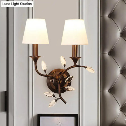 Antique brass two-light wall mount lamp with crystal leaf accents and cream fabric shades for bedroom decor