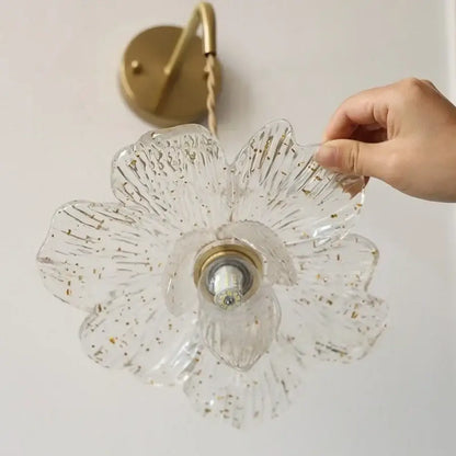 Clear glass flower-shaped led wall light with gold foil accents and antique brass mounting plate for bedroom sconce
