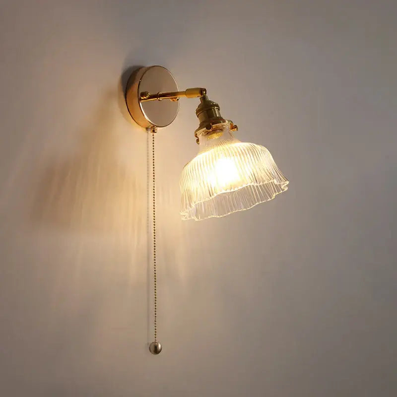 A warm-toned antique brass glass rotate copper wall sconce with ribbed translucent shade and pull-chain switch for bedroom