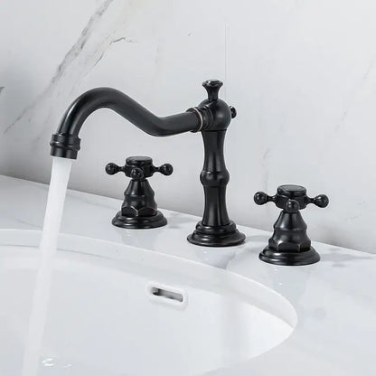 Black matte-finished brass three-handle bathroom faucet with ornate cross handles and gold finish curved spout