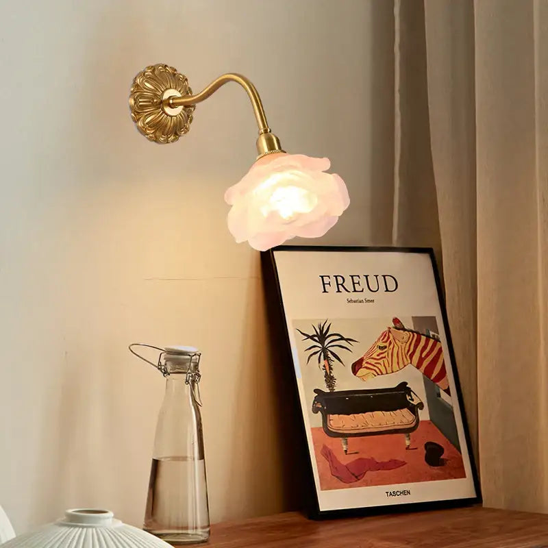 A delicate wall lamp with a decorbites copper arm and soft pink flower-shaped rose glass shade for bedroom decor