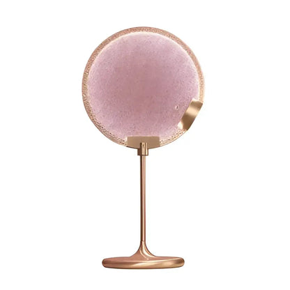 A round rose gold framed vanity mirror with a clear pink glass surface paired with decorbites clear pink pendant light